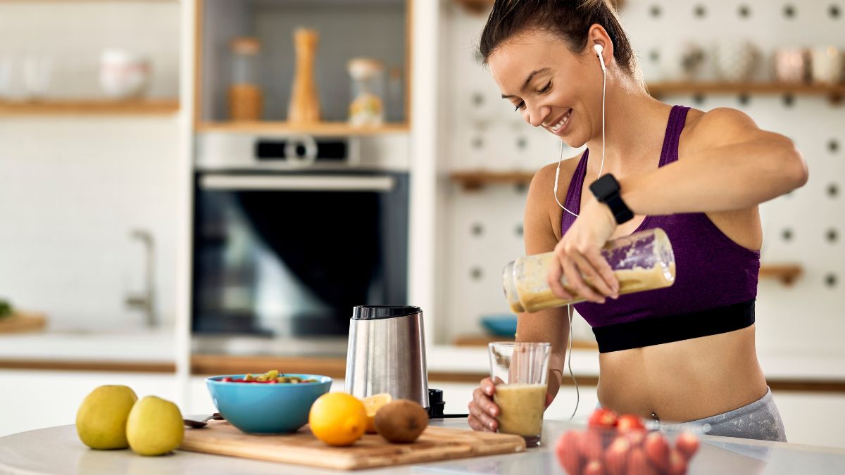 Woman making healthy smoothies in workout gear in her kitchen